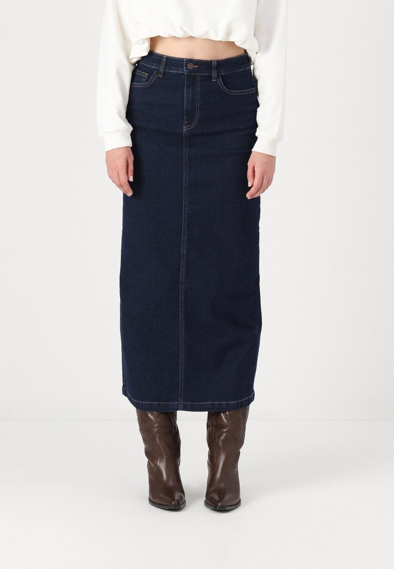 Σκούρο μπλε τζιν μίνι φούστα με μπροστινή ραφή, ψηλή μέση και ίσια γραμμή. Συνδυάζεται με καφέ μπότες μέχρι το γόνατο για αντίθεση.