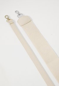 Zwei Riemen: einer aus strukturiertem, beigem Stoff mit geprägten Designs, der andere aus glattem, beigem Leder. Die Beschläge bestehen aus goldenen und silbernen Clips.