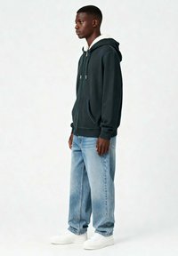 Tume roheline kapuutsiga pusa valge, pehme voodriga, ees taskud, koos helesiniste teksade ja valgete tossudega. Lihtne, igapäevane disain.