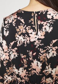 Black floral dress featuring a pattern in pink, beige, and deep red. Fastened at the back with a small button and loop detail. Soft, smooth fabric.