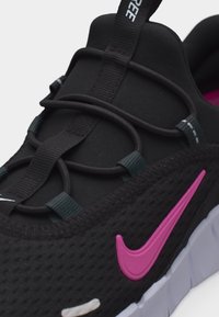 Chaussure de sport noire avec le swoosh Nike rose, lacets élastiques noirs et semelle blanche segmentée.