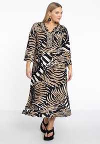 Maxikleid aus leichtem Material mit einem zebraähnlichen Muster in Schwarz, Beige und Weiß, dazu ein mit Perlen besetzter Ausschnitt und Dreiviertelärmel. Abgerundet mit schwarzen Plattformschuhen.
