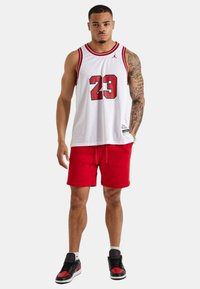 Hvid mesh basketballtrøje med rød kant og nummer 23, kombineret med røde shorts og sorte sneakers med røde detaljer.