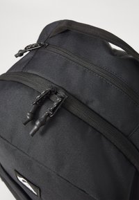Mochila de tela negra con dos compartimentos con cremallera, tiradores de cremallera resistentes y un detalle de superficie texturizada.