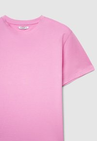 Maglietta rosa chiaro a maniche corte in cotone, con scollo tondo e tessuto liscio e morbido. L'etichetta riporta la scritta "CALLIOPE."