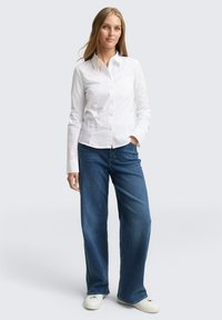 Witte overhemd met knoopsluiting en kraag, gecombineerd met blauwe wijde jeans en witte sneakers. Glad materiaal met rechte snit.
