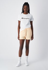 Biała bawełniana koszulka z logo "Champion", zestawiona z jasnoróżowymi szortami z elastycznym pasem i sznurkiem. Białe sneakersy i skarpetki w zestawie.