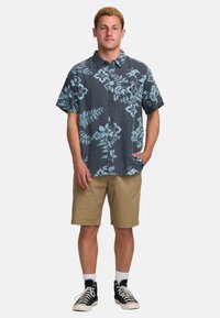 Camisa de manga corta de color azul oscuro con un patrón floral en azul claro, diseño de botones, combinada con pantalones cortos caqui y zapatillas negras.