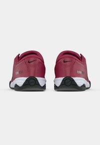 Sarkanie Nike apavi ar gludu sintētisku augšdaļu, ar melnu logotipu un baltu starpzoli. Profilā redzama noapaļota papēža forma un aprīkota ar gumijnu zoli.