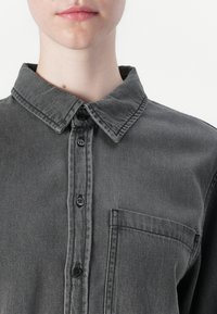 Grey denim shirt with a pointed collar, button front, and single chest pocket. Features a soft texture and faded appearance.