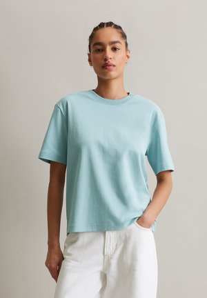 Light blue cotton T-shirt with short sleeves, crew neckline, relaxed fit, and subtle texture. Paired with white, high-waisted pants.