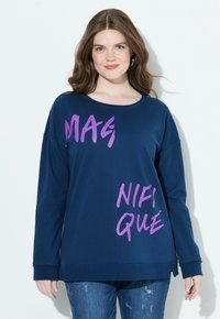 Felpa blu navy con testo grafico viola "MAGNIFIQUE." Presenta un collo rotondo, maniche lunghe e una vestibilità rilassata. Tessuto morbido.
