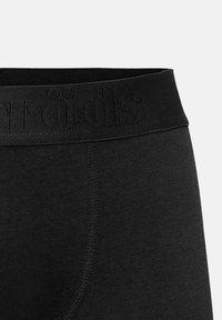 Fascia in tessuto elastico nero con il nome del brand leggermente in rilievo, cuciture verticali visibili su materiale morbido.