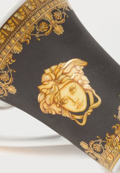 Μαύρο φλυτζάνι με περίτεχνο χρυσό φυτικό περίγραμμα και έμβλημα κεφαλής Μέδουσας από χρυσό στο κέντρο σε λευκό φόντο.