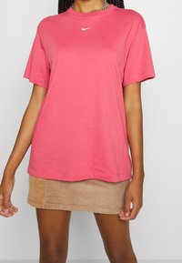 Rosa bomullströja med kort ärm och rund hals, med en liten vit Nike-logotyp på bröstet, i kombination med en beige kordfløyel mini kjol.