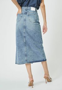 Denim midi krilo z nosom svetlo modre barve, zadnjimi žepi in ravnim silhuetom. Ima rob, ki sega tik pod kolena, in subtilno šivanje.