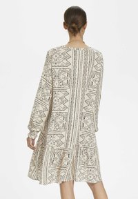 Kortärmad klänning i krämfärgad tyg med svarta geometriska mönster; har en rynkad midja och lös passform, som slutar ovanför knäet med en volangkant.