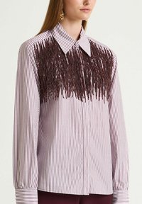 Camicia a righe con bottoni e maniche lunghe; presenta dettagli con frange color bordeaux sul petto. Tessuto morbido, colletto classico e polsini con bottoni.