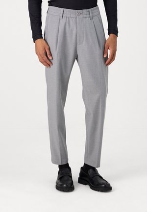 Helle graue, plissierte Hosen aus strukturiertem Stoff, mit Knopfverschluss und schmalem Schnitt, kombiniert mit schwarzen Schuhen und Socken.