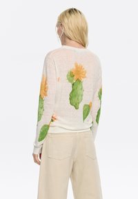 Lichte gebreide trui in crème met kleurrijke cactussen en bloemenprints. Heeft lange mouwen en een relaxte pasvorm bij de taille.