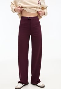 Bordeaux brede broek gemaakt van een gladde stof, met een enkele knoopsluiting en twee voorzakken. Gepaard met neutrale sneakers.