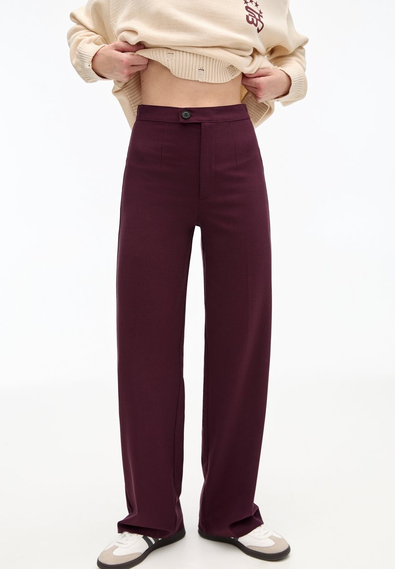 Bordeaux brede broek gemaakt van een gladde stof, met een enkele knoopsluiting en twee voorzakken. Gepaard met neutrale sneakers.