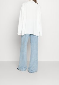 Maglietta bianca, oversize, a maniche lunghe con vestibilità comoda, abbinata a jeans in denim baggy di colore azzurro chiaro con orlo sfilacciato.