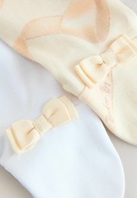 Divas zeķu pāri: viens persiku krāsā ar mīkstu rakstu un loku, otrs balts ar ribotu dzeltenu loku. Abu izgatavoti no mīksta auduma.