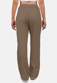 Braune, strukturierte, weit geschnittene Hosen mit elastischem Bund. Der Stoff hat ein zerknittertes Muster, das eine entspannte Passform bietet. Getragen mit einem weißen Cropped-Top.