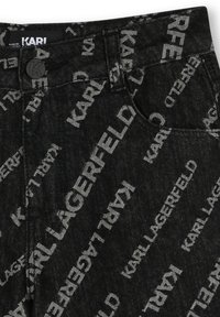 Pantalon en denim noir avec un motif logo blanc répétitif. Taille haute avec une fermeture à bouton et des poches standard. Texture durable.