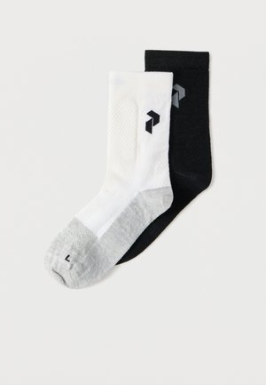 Egy pár zokni, egyik fehér szürke orral és fekete logóval, a másik egyszínű fekete, hozzáillő szürke logóval, fehér háttéren szétterítve.