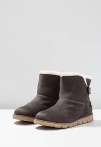 Harmaat mokkasiinipohjaiset nilkkasaappaat, joissa on tekoturkisvuori, litteä kumipohja ja koristeellinen sivulukko.