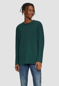 Groene katoenen t-shirt met lange mouwen, een ronde hals, een relaxte pasvorm en een rechte zoom, gecombineerd met blauwe spijkerbroeken.