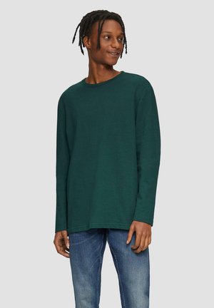 Langärmliges grünes Baumwoll-T-Shirt mit rundem Halsausschnitt, lockerer Passform und geradem Saum, kombiniert mit blauen Jeans.