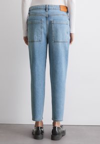 Lys blå denim jeans med avsmalnende ben, to baklommer og en oransje skinnlapp p�å linningen. Indre sømmer er ferdigstilte.