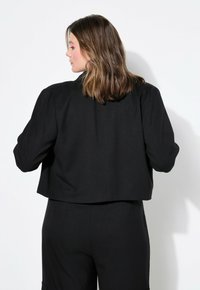 Giacca nera corta con un design strutturato, dotata di maniche lunghe, una texture liscia e senza hardware o accenti visibili.