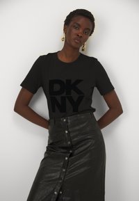 Musta puuvillapaita, jossa on suuri musta DKNY-logotipoika, yhdistettynä korkeavyötäröiseen mustaan nahkahameeseen, jossa on nepparikiinnitys ja sivutaskut.