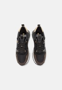 Par de zapatillas negras y marrones con acentos dorados, cordones y la marca Michael Kors, exhibidas desde una vista superior sobre un fondo blanco.