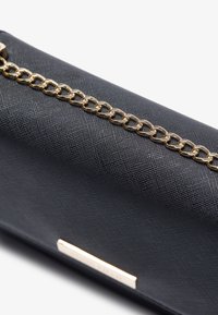 Svart texturerad kuvertväska i syntetmaterial med ett guldmetallkedjehandske och en rektangulär guldaccent.