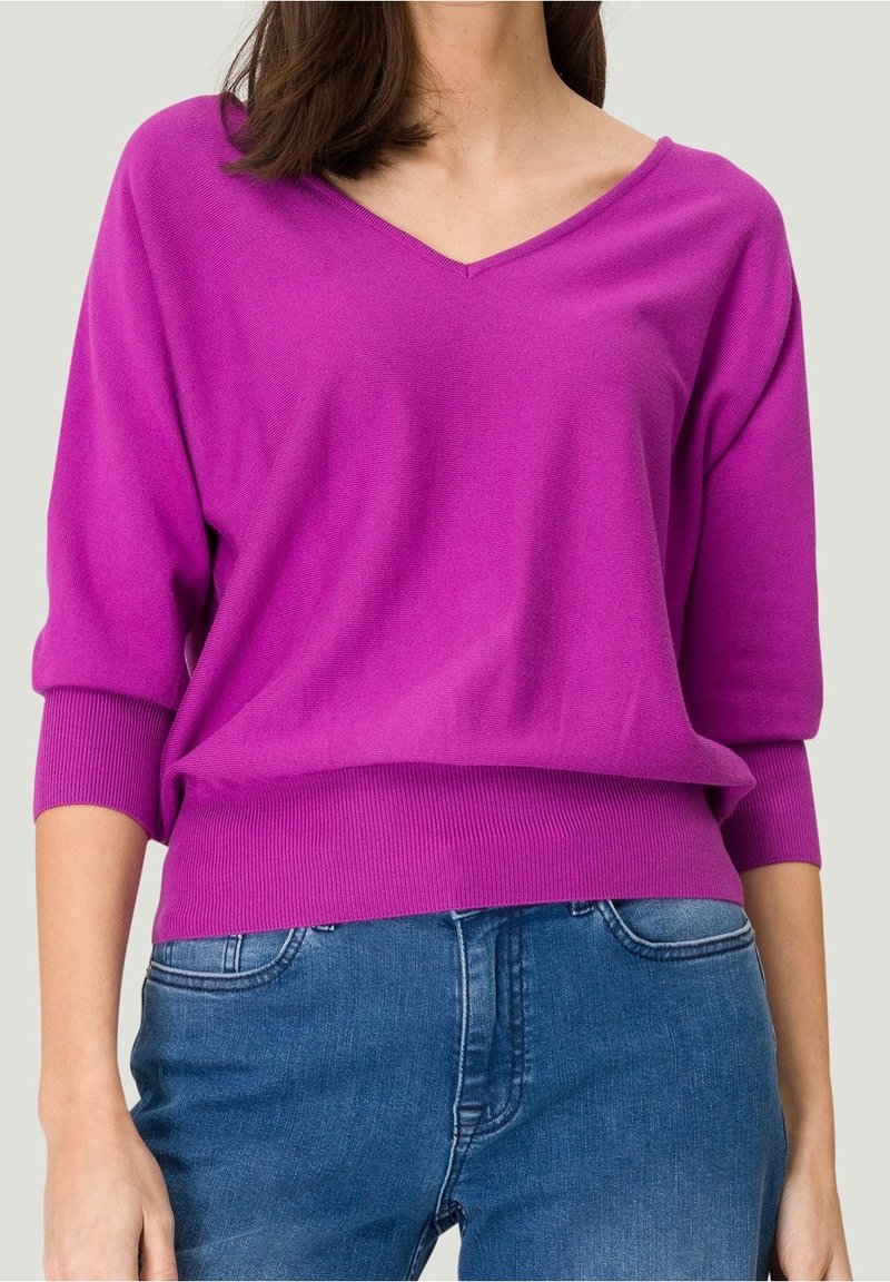 Maglione oversize a V in tonalità rosa brillante, realizzato in maglia, con polsini e orlo a coste, abbinato a jeans blu. Design casual classico.