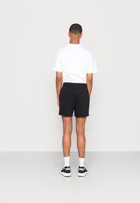 Shorts noirs avec une taille élastique et une poche arrière, associés à un t-shirt blanc à manches courtes unis et des chaussures de sport.