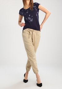 Camiseta navy con estampado floral, combinada con pantalones jogger beiges que cuentan con una cintura elástica y puños, llevados con tacones altos negros.