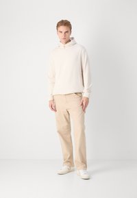 Sudadera color beige claro con capucha, de manga larga y puños acanalados, combinada con pantalones beige claros. Zapatillas blancas completan el atuendo.