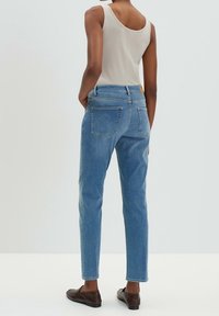 Vaaleansiniset farkut suoralla lahkeella, korkealla vyötäröllä ja kahdella takataskulla, yhdistetty beigen väriseen toppiin ja ruskeisiin jaloissa oleviin tasapohjaisiin kenkiin.