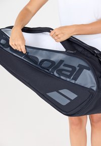 Borsa sportiva nera con apertura con zipper, interno liscio e un logo prominente. Presenta un tessuto resistente e un design minimalista.