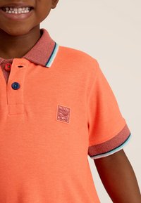 Korte mouw polo in fel oranje katoen met een gestructureerde kraag, blauwe en groene afwerking, en een klein logo op de borst.