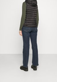 Svart pufferväst med huva över en mörkgrön långärmad tröja, i kombination med blå rakbenjeans och svarta kraftiga stövlar.