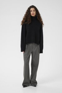 Black, oversized knitted sweater with a high collar, paired with gray, wide-leg trousers. Smooth texture and relaxed fit, minimal detailing.