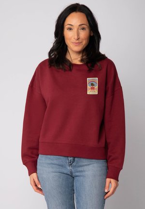 Bordeaux sweatshirt met een ontspannen pasvorm, voorzien van een bedrukte voorzijde. Zacht materiaal, wijde mouwen en geribbelde zoomdetails.