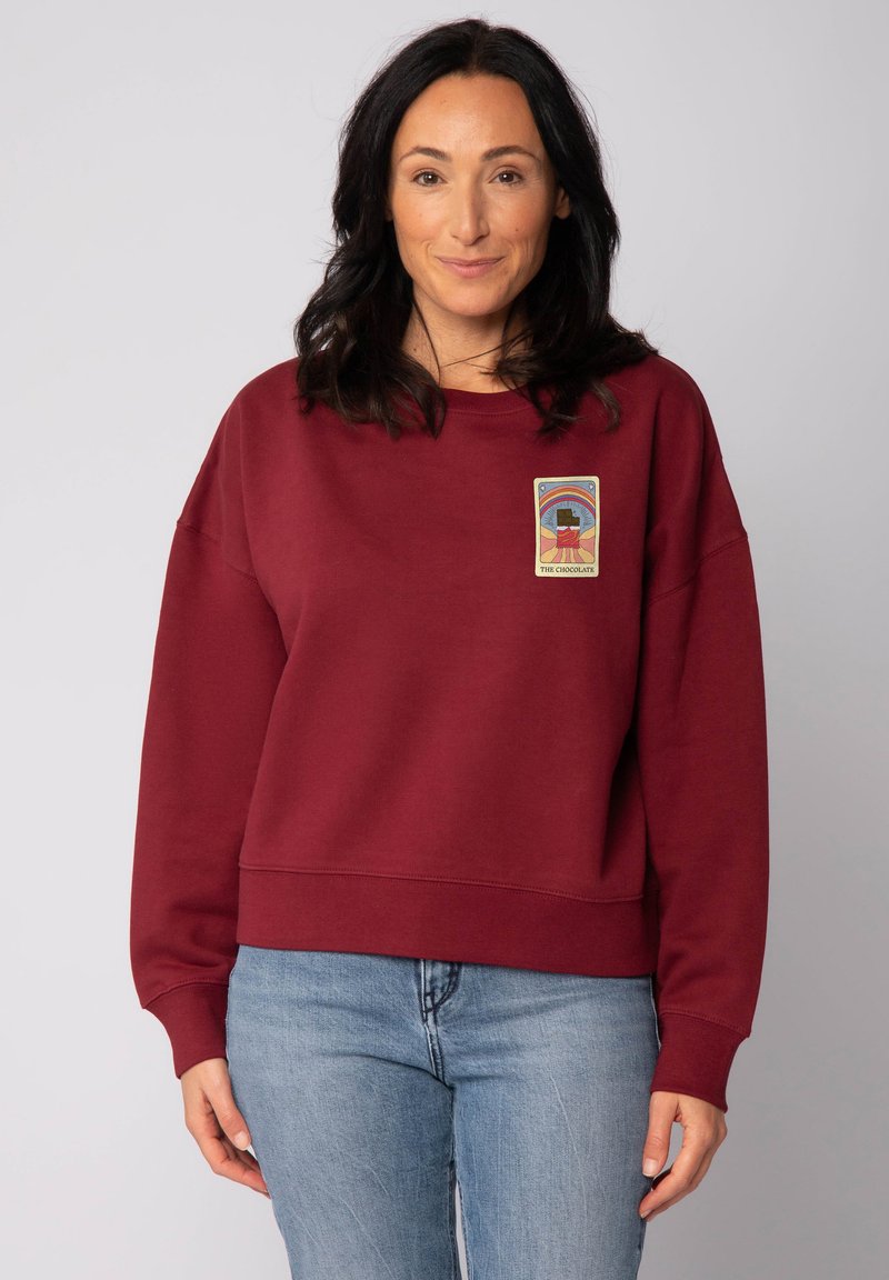 Sweatshirt bordeaux à la coupe décontractée, avec un motif imprimé sur le devant. Tissu doux, manches larges et bord-côte en détail.